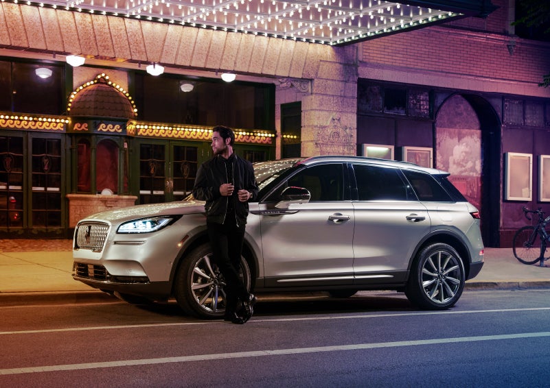A 2022 Lincoln Corsair SUV is parked outside a theater as the driver relaxes against the frame and lights illuminate the floating roofline and body | Mark Ficken Lincoln in Charlotte NC