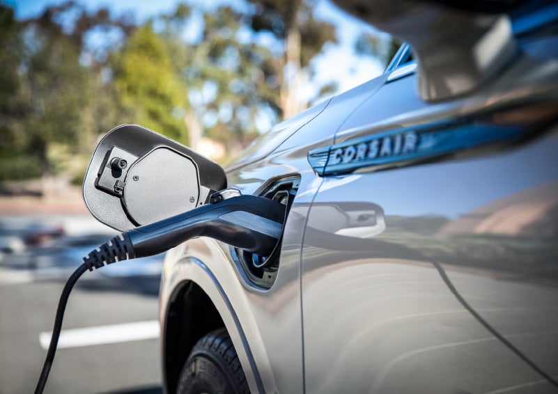 A Lincoln electric charger is plugged into a 2022 Lincoln Corsair Grand Touring port as the body reflects the surroundings of a sun-soaked parking lot | Mark Ficken Lincoln in Charlotte NC