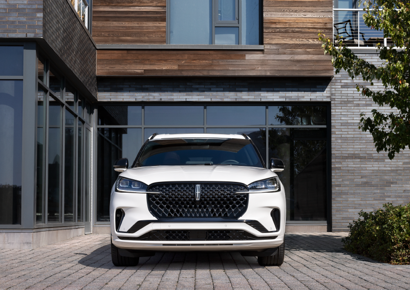 A white 2025 Lincoln Aviator® SUV is shown parked outside a modern building with gray brick and wood accents. | Mark Ficken Lincoln in Charlotte NC