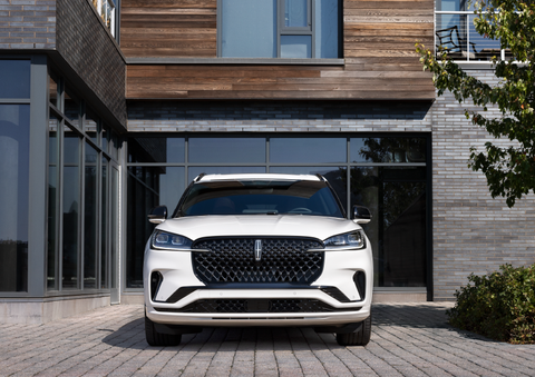 A white 2025 Lincoln Aviator® SUV is shown parked outside a modern building with gray brick and wood accents. | Mark Ficken Lincoln in Charlotte NC