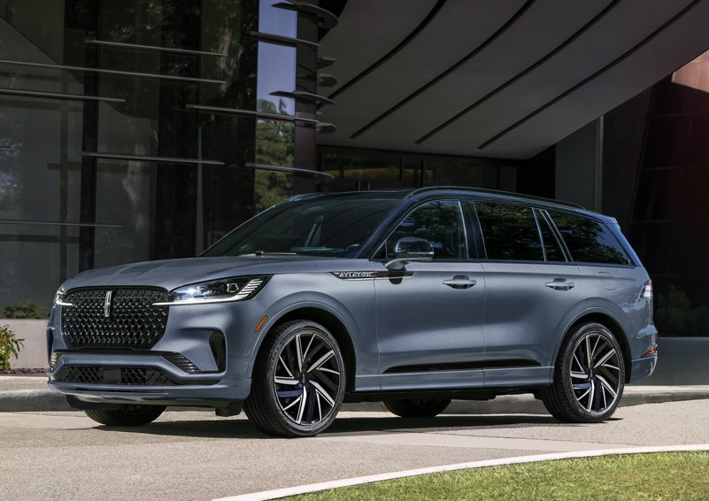 A gray 2025 Lincoln Aviator® SUV is parked outside a modern building showcasing the driver’s side of the vehicle. | Mark Ficken Lincoln in Charlotte NC