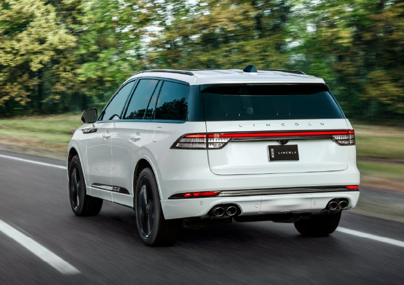 A white 2026 Lincoln Aviator® SUV is being driven away down a road lined with colorful trees. | Mark Ficken Lincoln in Charlotte NC
