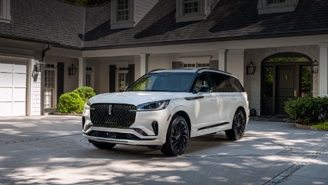 A white 2026 Lincoln Aviator® SUV is parked in the driveway of a luxury home. | Mark Ficken Lincoln in Charlotte NC